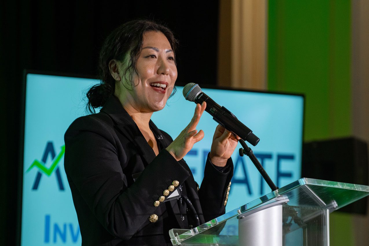 A woman is speaking at an event with microphone.